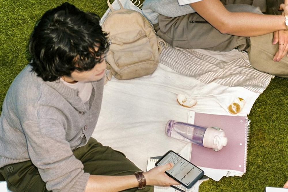 Dos personas estudiando al aire libre con un teléfono y cuadernos