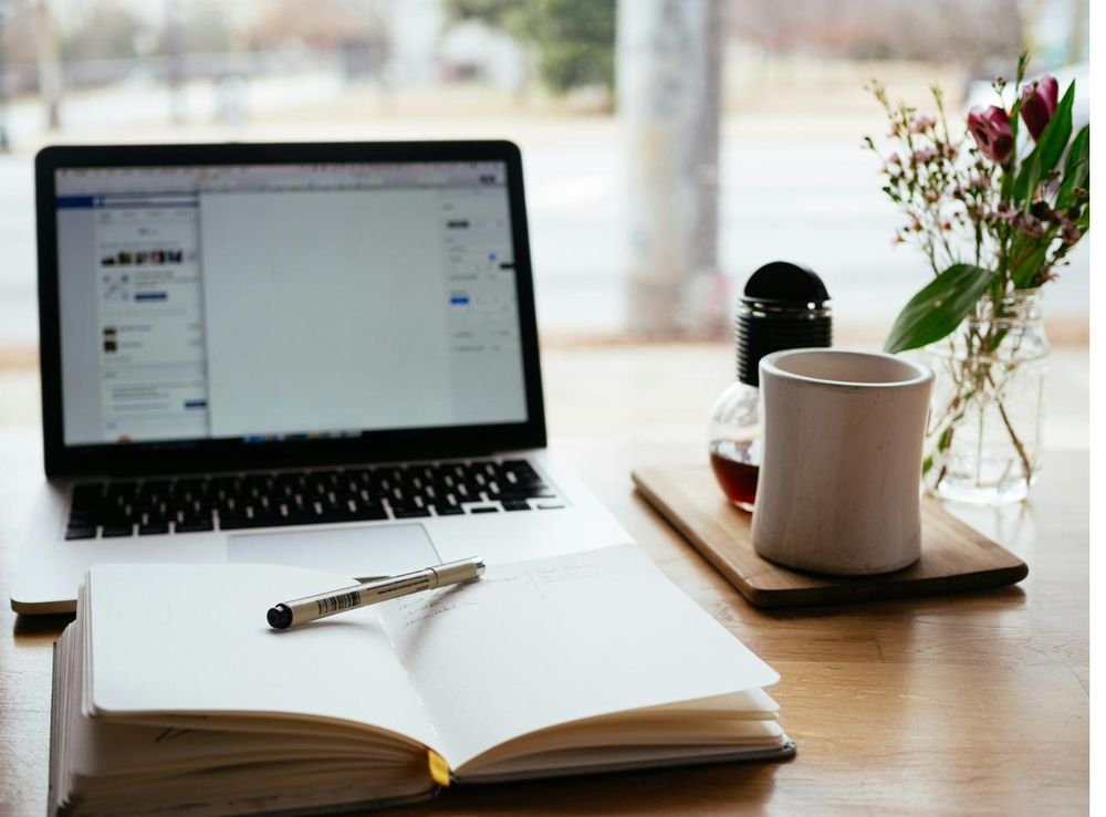 Computador portátil junto a un cuaderno abierto y una taza de café