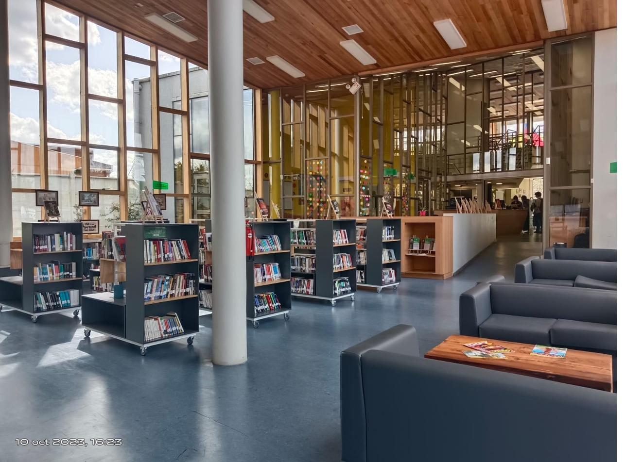 Interior luminoso de una biblioteca pública con estanterías de libros y zona de lectura