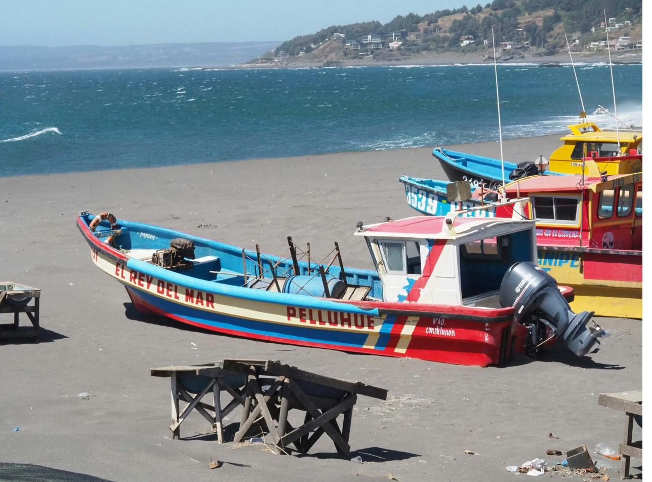Botes de pesca artesanal de colores varados en una playa de arena, con el mar y la costa al fondo