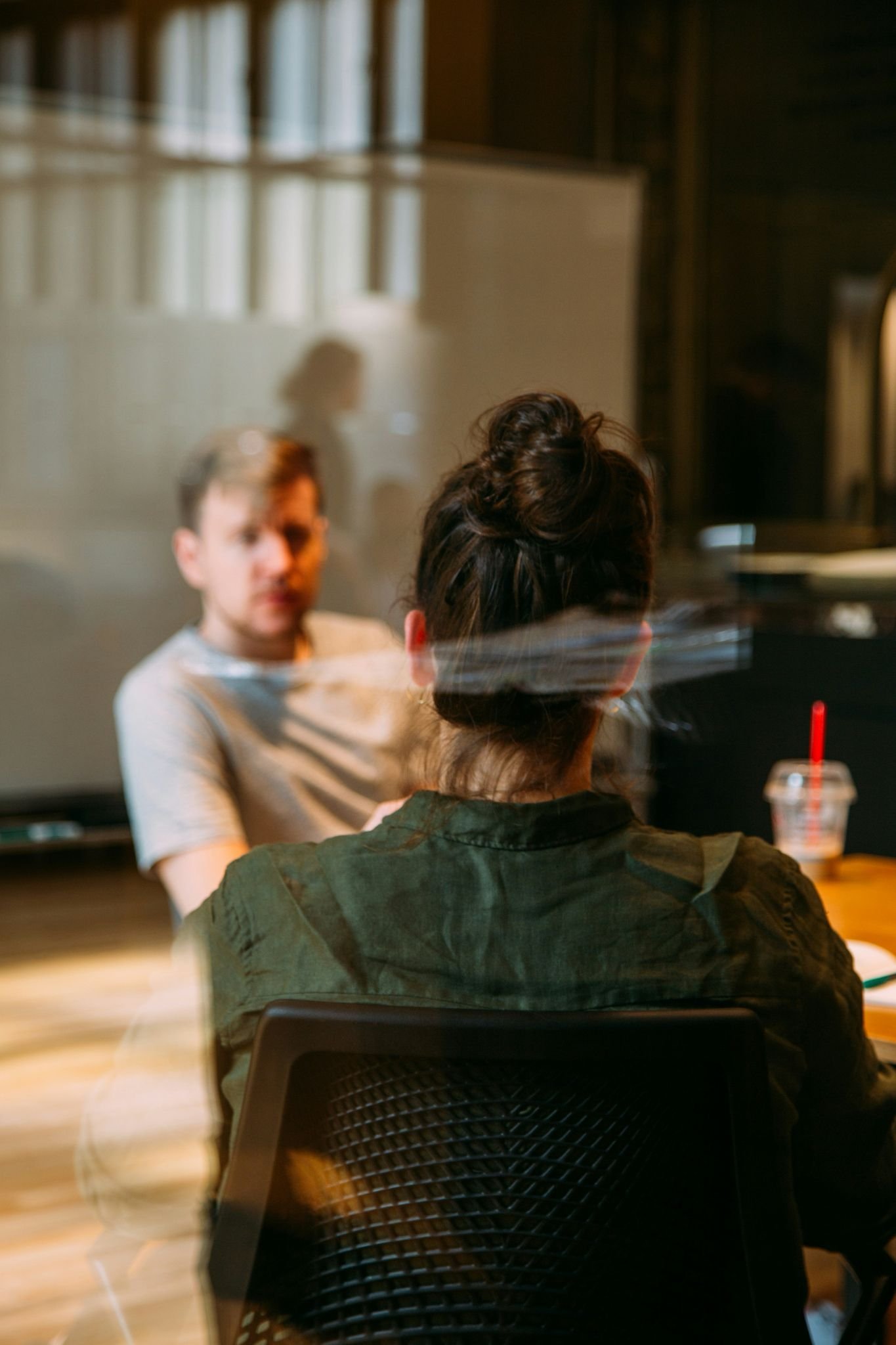 Conversación de trabajo entre dos personas en un espacio interior, observada a través de un vidrio con reflejos